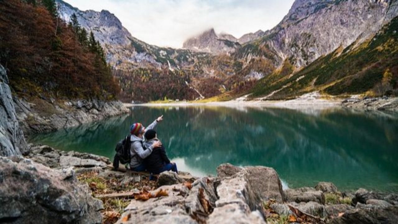 A couple sitting in the valley of mountains in front of a large body of water. 