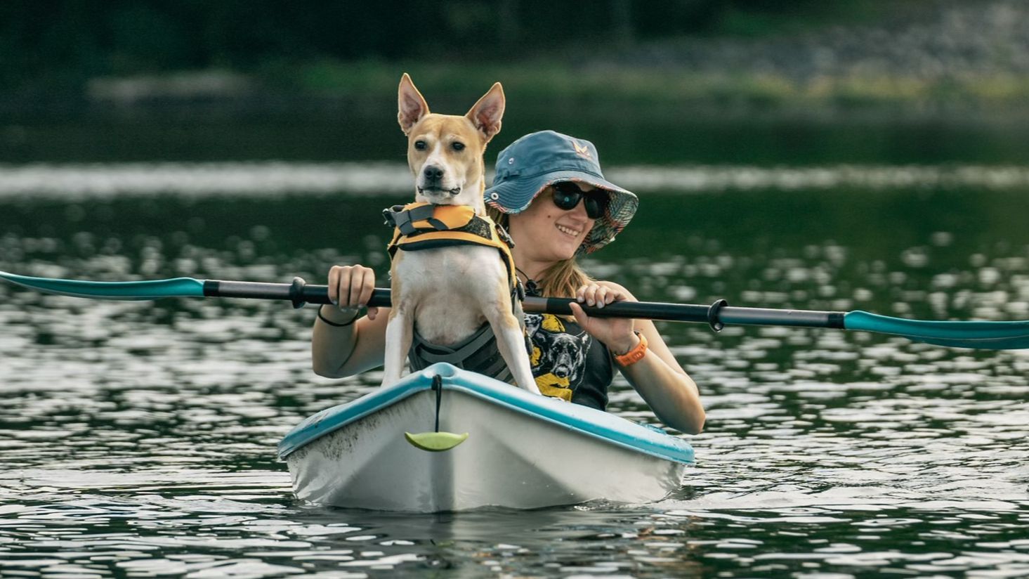 Woman wearing bucket hat paddling kayak with mixed breed dog wearing a lifejacket