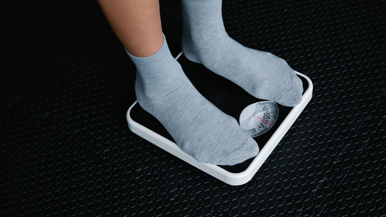 Feet in grey socks standing on a white bathroom scale on a dark textured floor