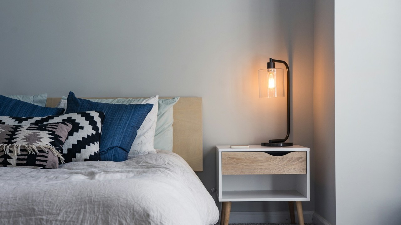 Soft morning light in a quiet bedroom with rumpled white duvet and warm bedside lamp