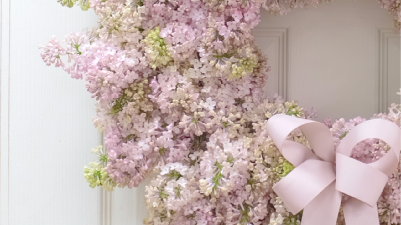 Soft pink lilac wreath by Joseph Massie, featuring abundant spring lilac blooms and a pale blush ribbon bow, styled on a white door as an elegant floral installation showcasing seasonal floral design and refined craftsmanship.