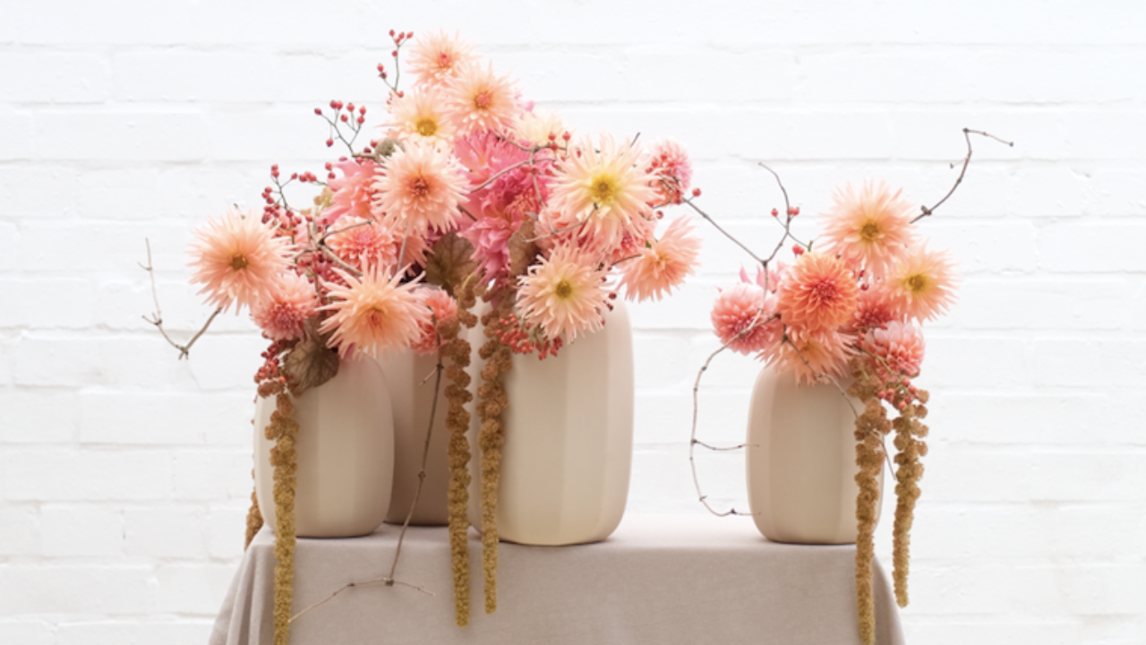 Luxurious hatbox arrangement of deep red garden roses, ranunculus, and textural seed pods in a sleek black container. A rich, romantic floral design by Joseph Massie, blending bold colour, lush texture, and contemporary elegance.