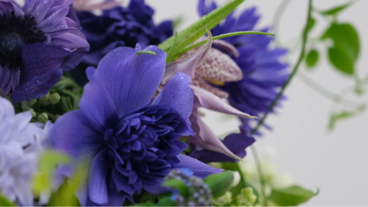 Close-up of a monochromatic blue bouquet featuring deep blue anemones, fritillaria meleagris and soft spring foliage, showcasing layered tones and texture.