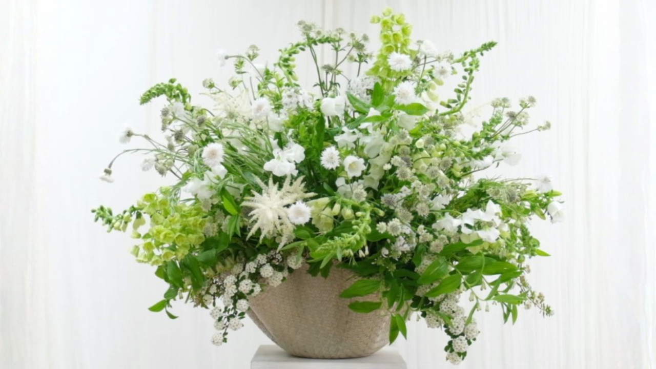 “A Basket of Joy”: a fresh, garden-inspired floral arrangement from Flower Class by Joseph Massie, featuring white and green seasonal blooms including astilbe, snapdragons, and foliage in a woven basket. A light, airy design celebrating natural movement, texture, and the beauty of seasonal flowers.