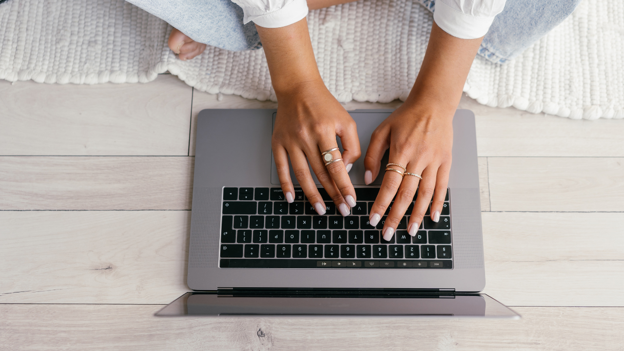 Woman sitting on the floor with her hands on her laptop.