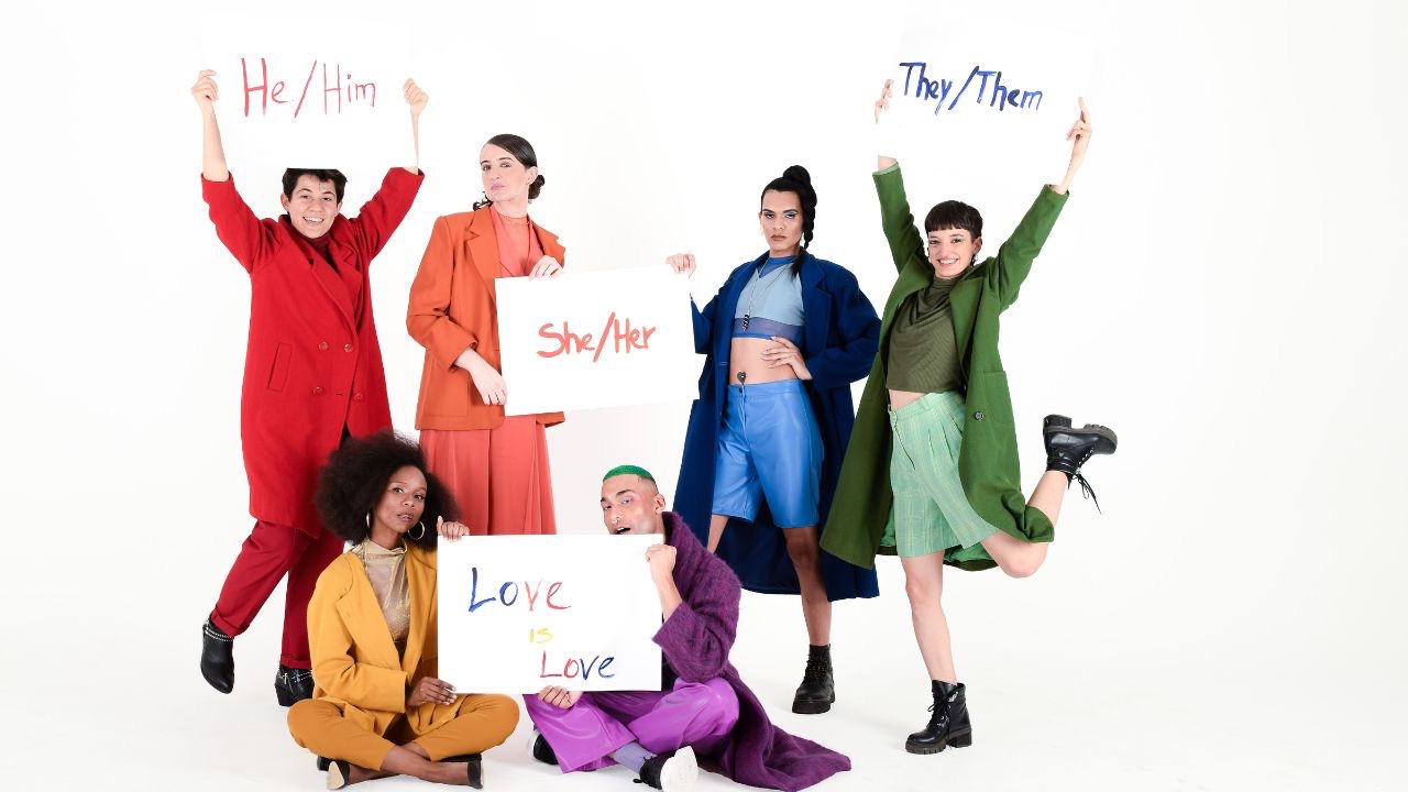 Image is of six people in an assortment of rainbow colored clothing holding up different signs that ready he/him she/hers they/them and love is love.  Being non-binary means something different for everyone and what it means for your child is different than what it might mean for my child. 