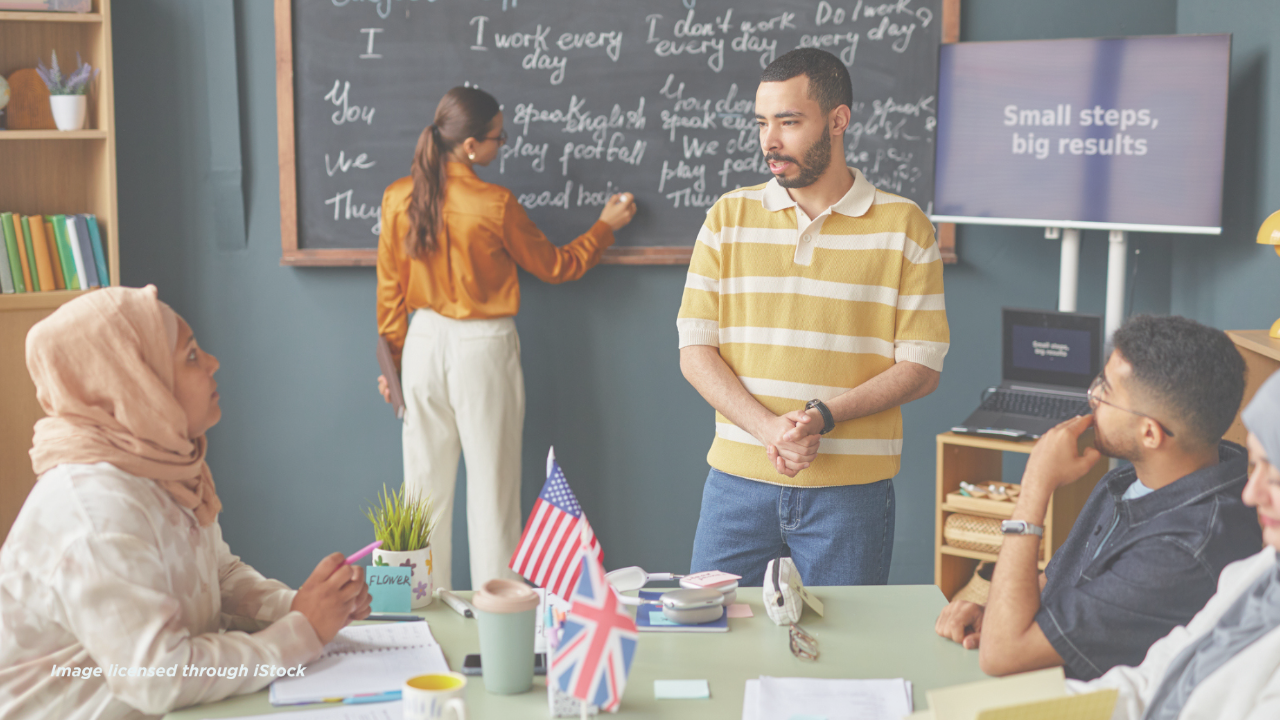 An instructor leading a diverse group of adult ESL students in a modern classroom, focusing on English learning goals written on a chalkboard.