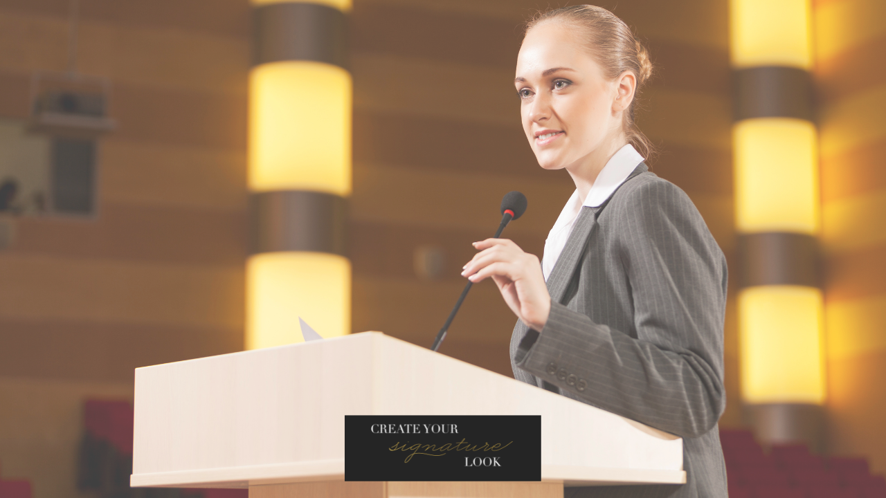 Image of a poised and self-assured woman takes the stage, elegantly clad in a suit, and firmly grasping the microphone. Her presence commands attention and exudes confidence.