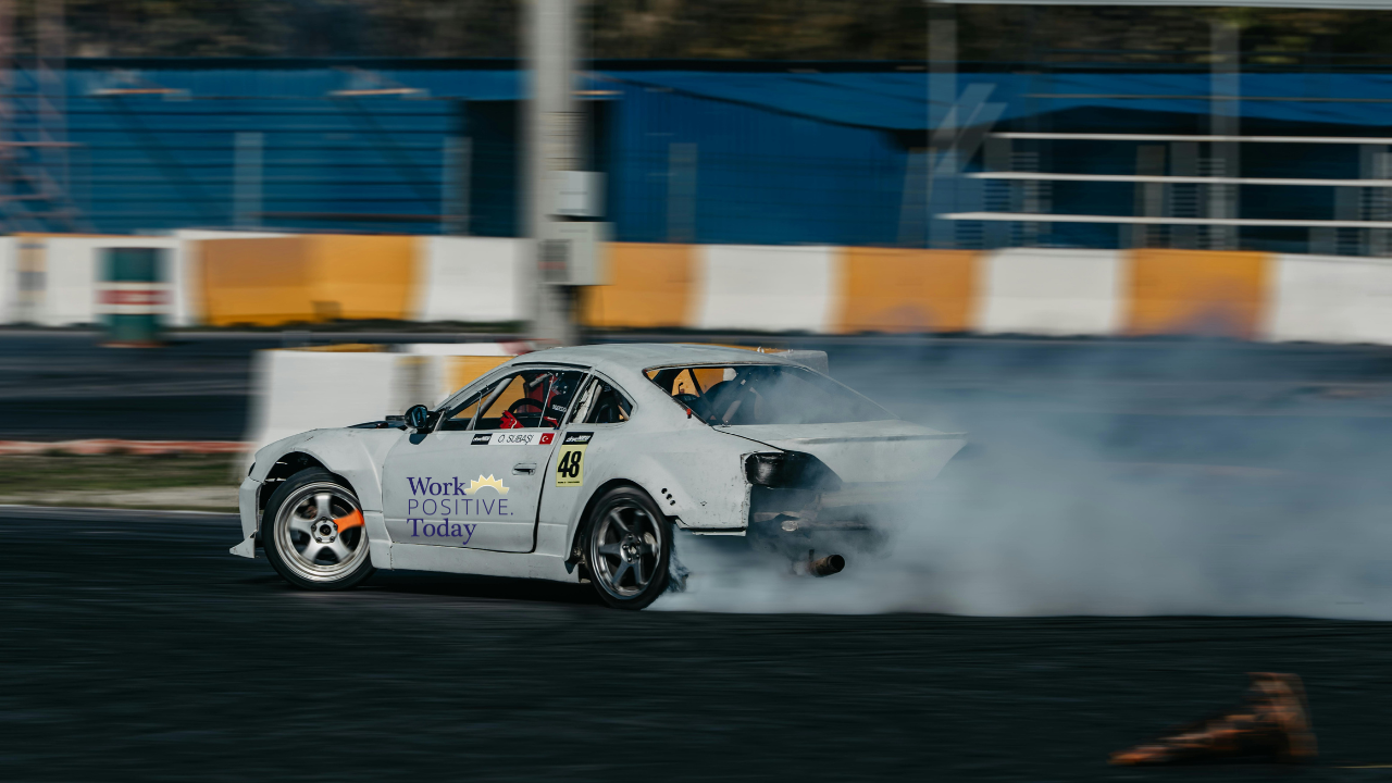 White race car number 48 with Work Positive Today logo speeding on professional racetrack with motion blur and tire smoke, demonstrating high-velocity performance and competitive advantage, illustrating the race to develop talent where learning velocity separates winners from whiners and 94% of employees stay longer when companies invest in fast-paced skill development.