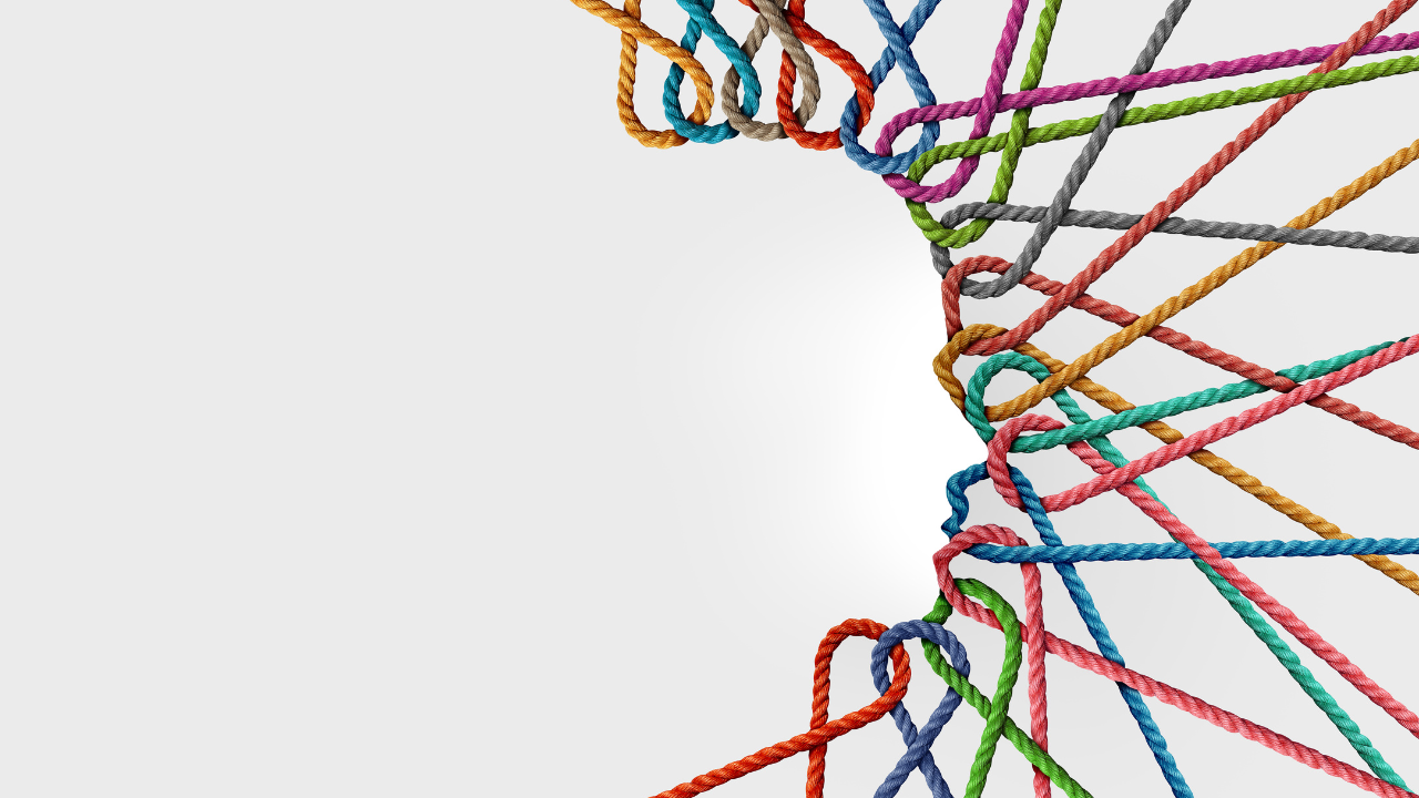 Multiple colorful ropes in orange, blue, red, green, pink, and gray intertwined and knotted together on white background, representing the complex interconnection of Mind, Body, and Business dimensions in holistic workplace performance and the productivity paradox of fragmented versus integrated approaches.