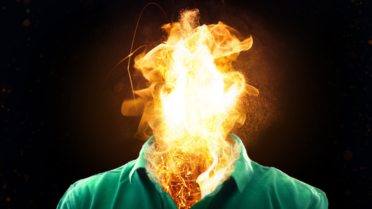 Person in green jacket with head engulfed in bright orange and yellow flames against dark background, dramatically illustrating employee burnout, workplace stress, and the destructive consequences of ignoring the Mind-Body-Business connection in performance management.