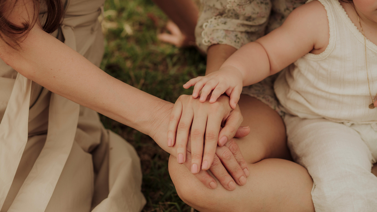 Close-up of a family’s hands stacked together outdoors — a parent and child joining hands, symbolizing teamwork, connection, and everyone playing their part at home.
