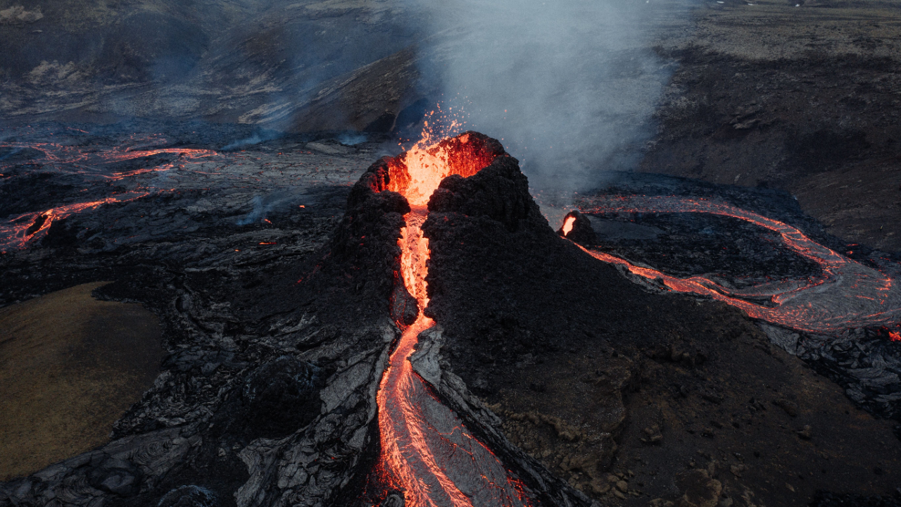 A dark volcano oozes and spouts out glowing orange lava with rivers of lava around it.