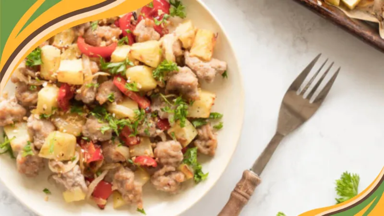 Plate of sheet pan pork with diced potatoes, red peppers, onions, and chopped parsley on a light surface, with a fork to the right and decorative green, gold, and brown curved border accents in the top left and bottom right corners.