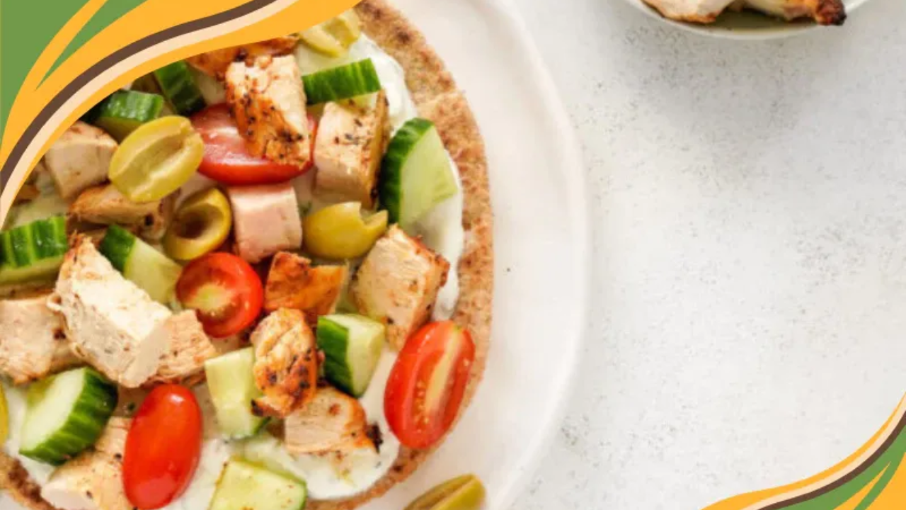 Grilled chicken pita topped with cucumbers, cherry tomatoes, olives, and a creamy spread on a white plate.