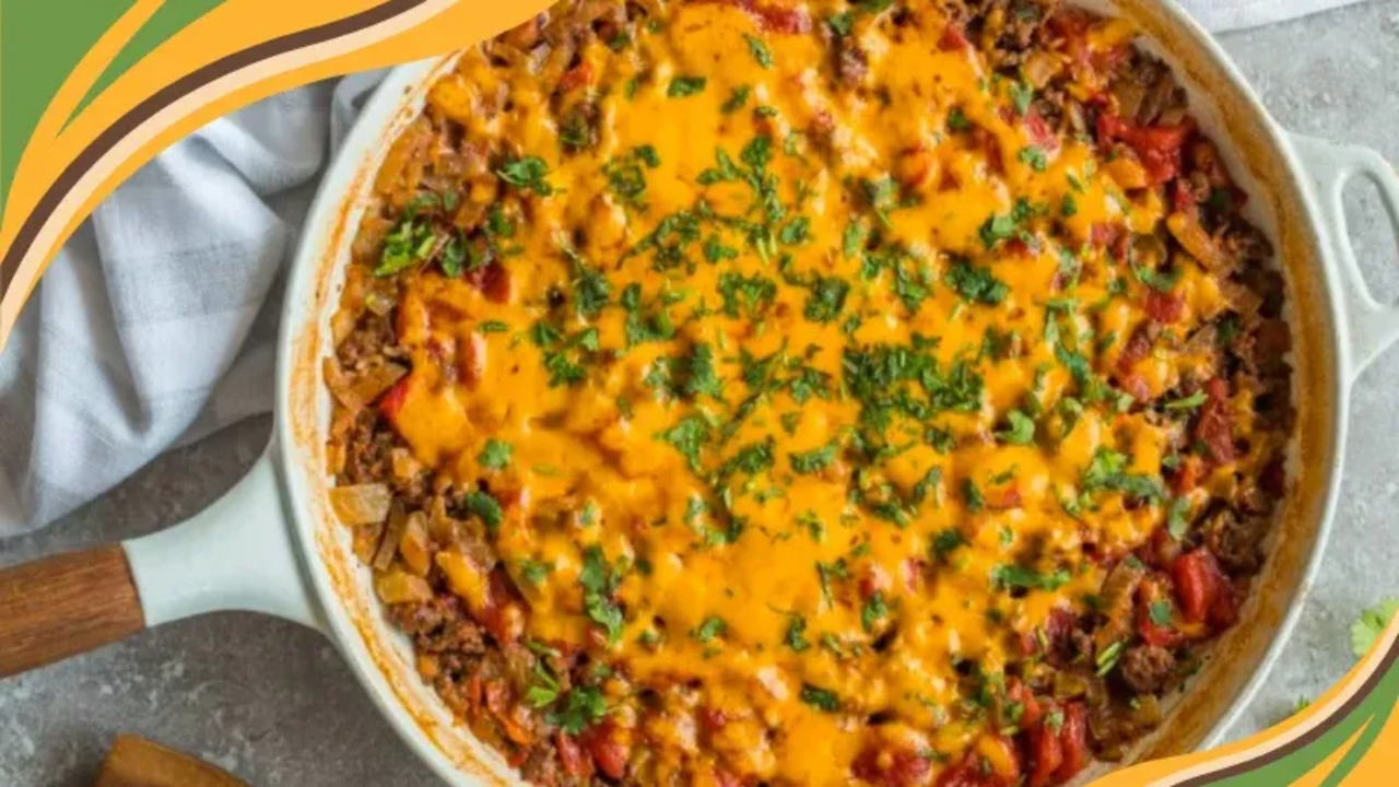 A one-pan burrito casserole in a white skillet with a wooden handle, topped with melted cheddar cheese and fresh chopped cilantro, resting on a gray stone surface next to a white striped towel.