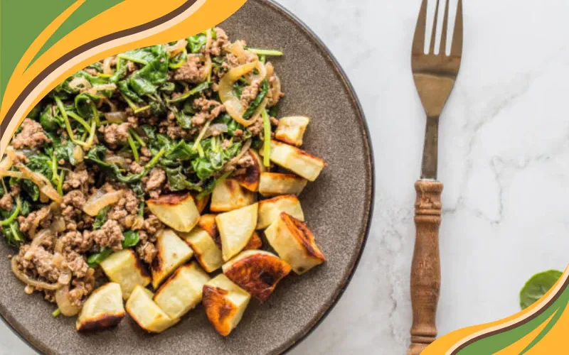 Ground beef sautéed with onions and greens, served with roasted golden sweet potatoes on a dark ceramic plate.