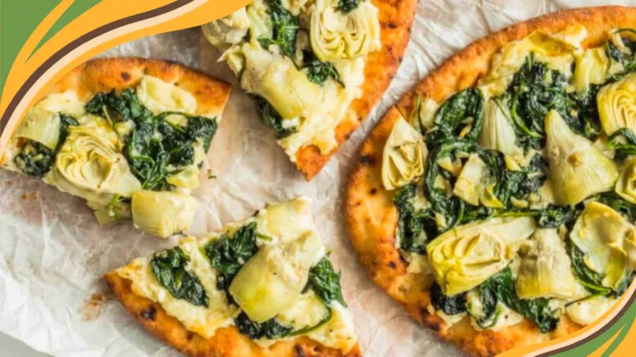 Two spinach and artichoke naan pizzas on parchment, golden brown and bubbling with melted cheese, topped with wilted spinach and chopped artichokes, resting on a rustic wooden surface.