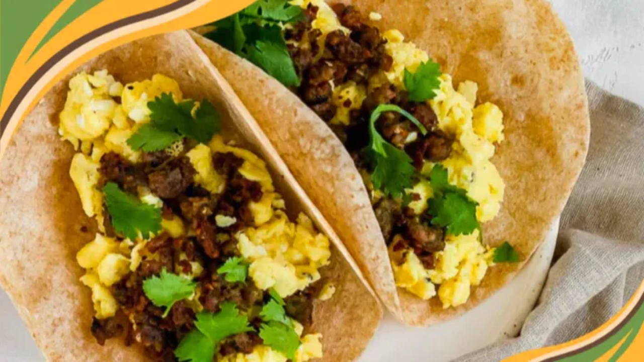 Two brown rice tortillas filled with scrambled eggs, cooked chorizo, and fresh cilantro, arranged on a white plate with a neutral linen napkin on a textured white background.
