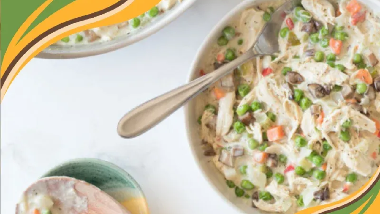 A bowl of crustless chicken pot pie filled with shredded chicken, peas, carrots and mushrooms in a creamy sauce, shown up close on a light surface.