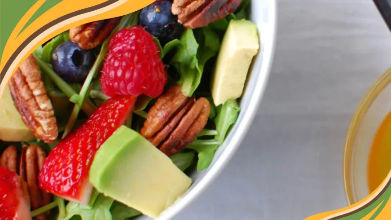 Fresh berry avocado salad with pecans and greens, served with a side of golden vinaigrette dressing.