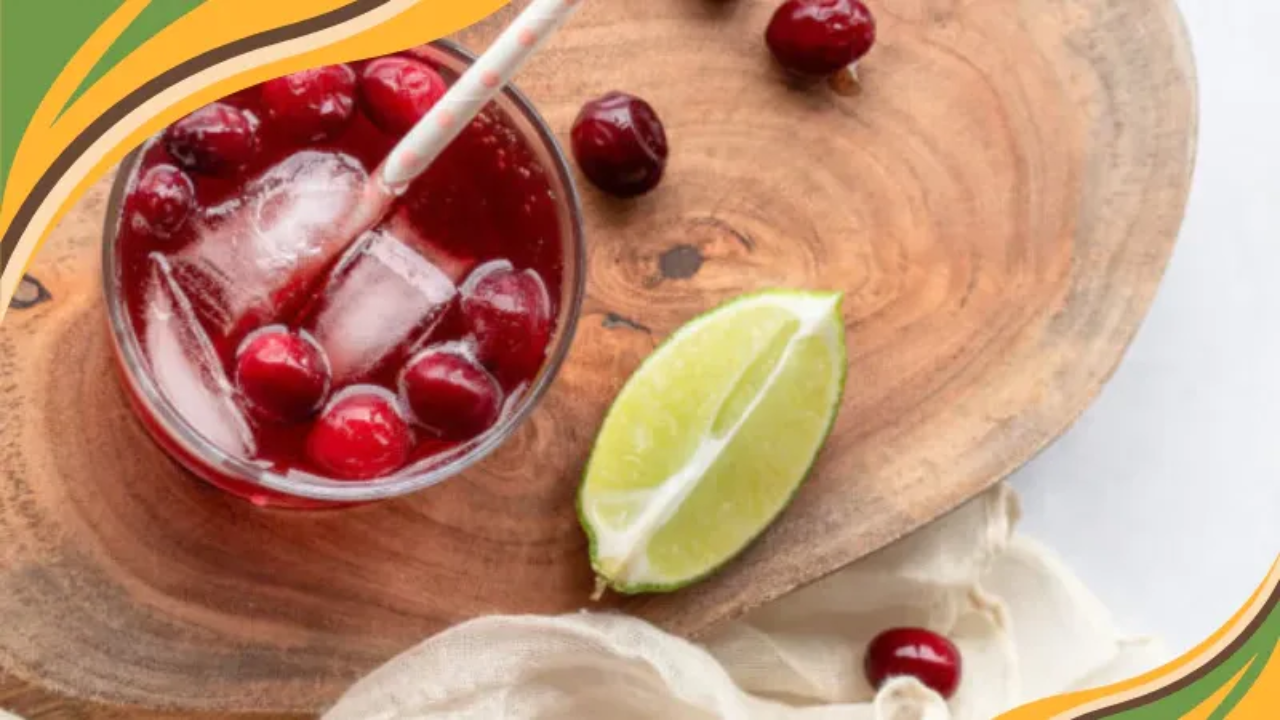 Refreshing cranberry cocktail with ice, whole cranberries, and lime wedge on a wooden serving board.