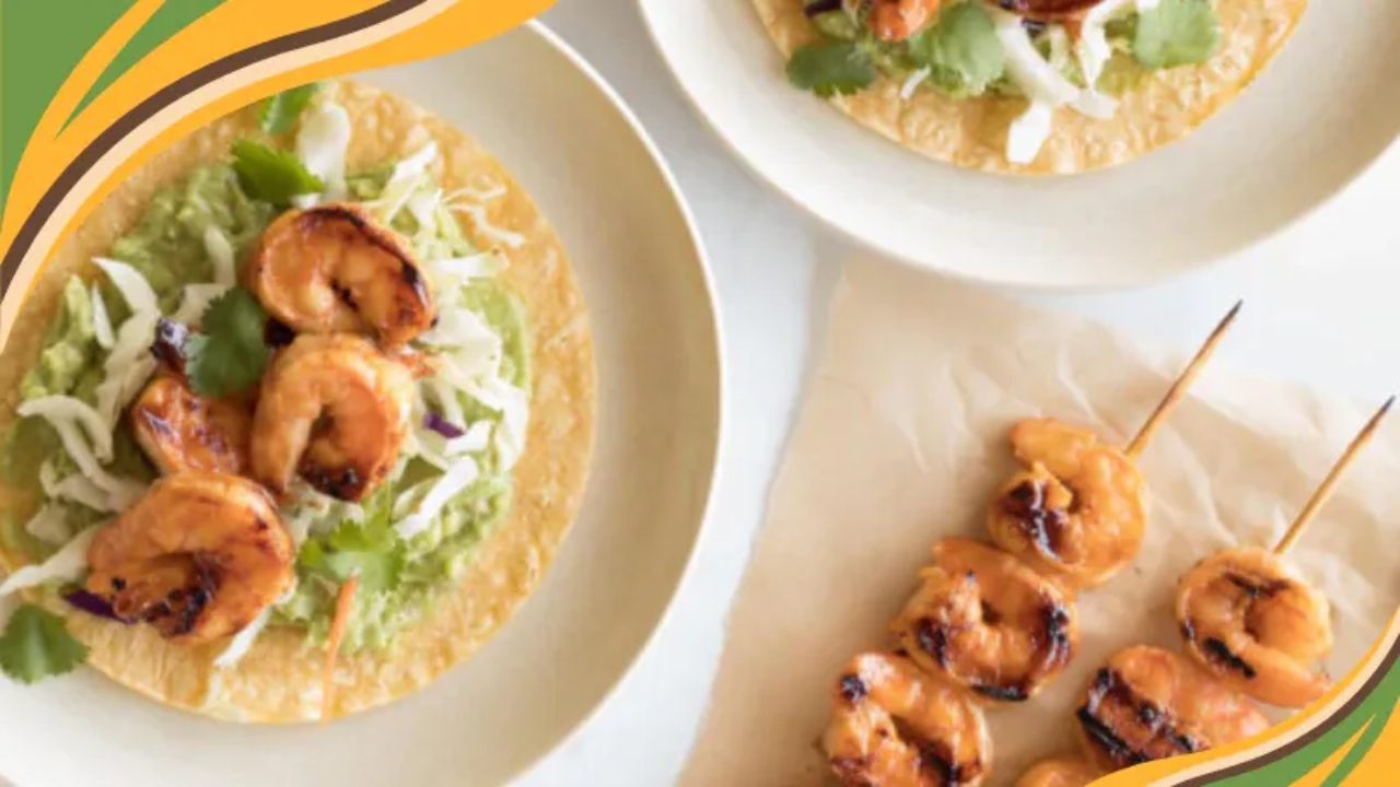 A plate of vibrant shrimp tacos filled with grilled shrimp, fresh cabbage slaw, avocado slices, and a drizzle of creamy sauce, served with lime wedges on a rustic table. 