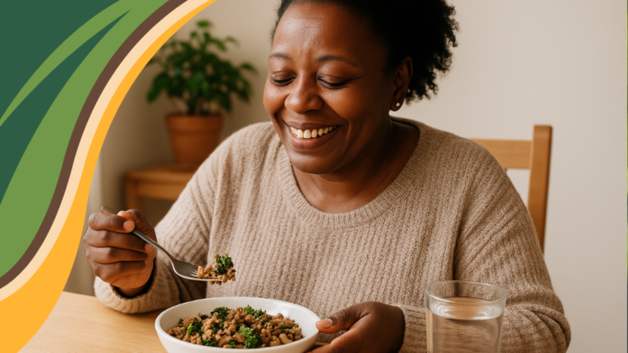 An African American woman in her 50s enjoys a home-cooked meal at her kitchen table, smiling with warmth and contentment. The cozy scene, lit by natural light and surrounded by earthy tones and greenery, reflects GRWL’s compassionate approach to conscious eating and sustainable weight loss through real food and joyful nourishment.