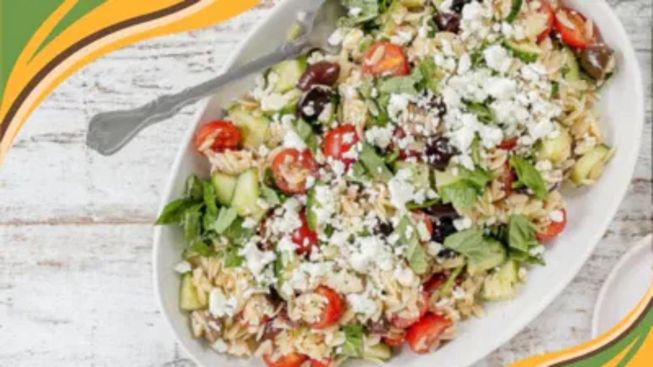 Fresh Greek orzo salad with cherry tomatoes, cucumbers, olives, and feta cheese, served on a white platter.