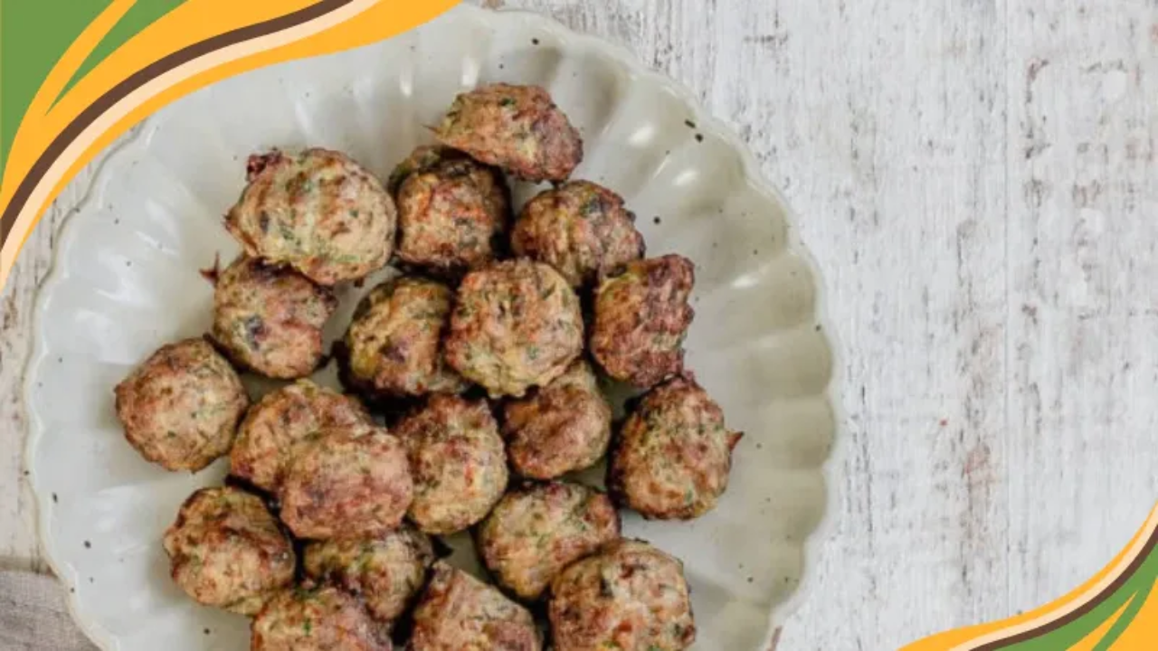 Plate of golden-brown homemade meatballs garnished with herbs, served on a rustic white wooden table.