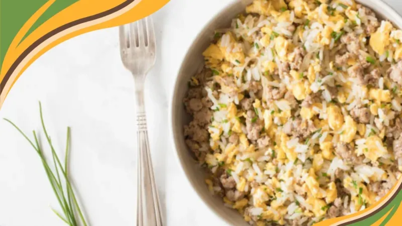 Bowl of sausage and egg fried rice with chives on a white surface, shown from above, with a fork beside it.