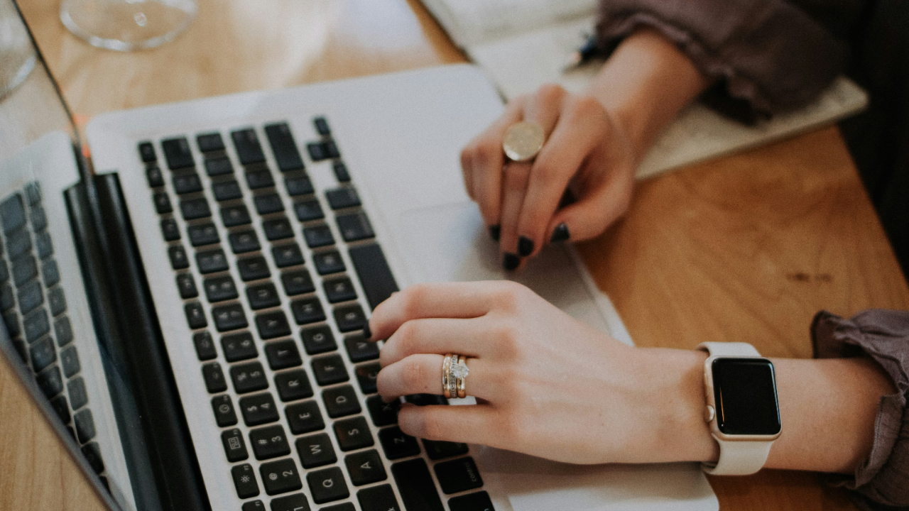 Hands typing on laptop with smartwatch and notebook nearby