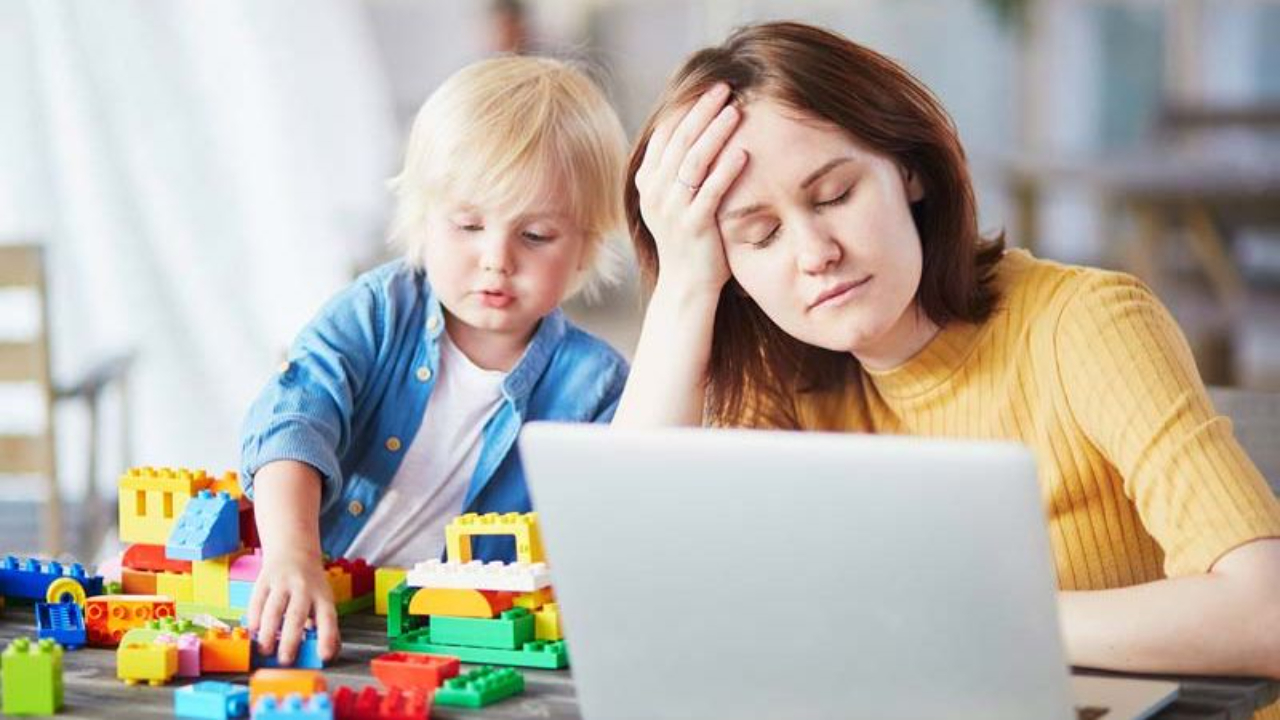 mom with her head in her hand while her toddler plays next to her