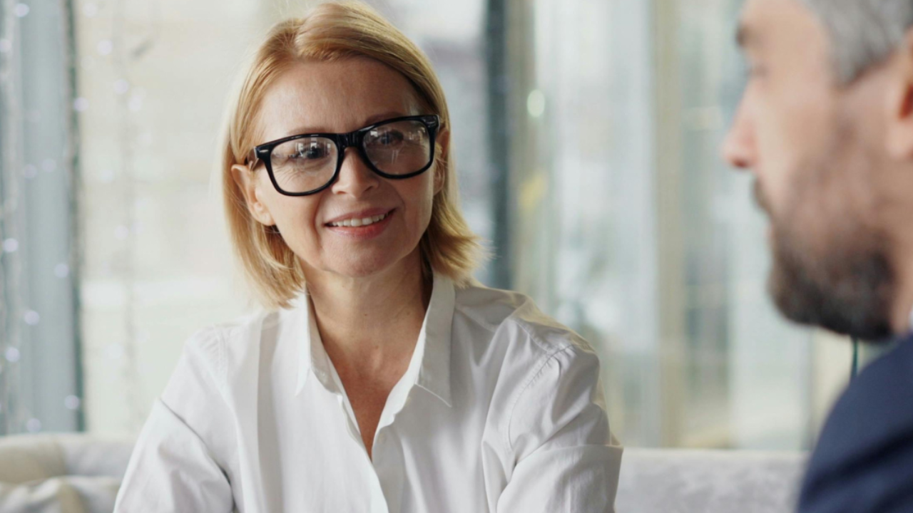 Photo of woman with short blonde hair and black glasses in a white button down shirt.