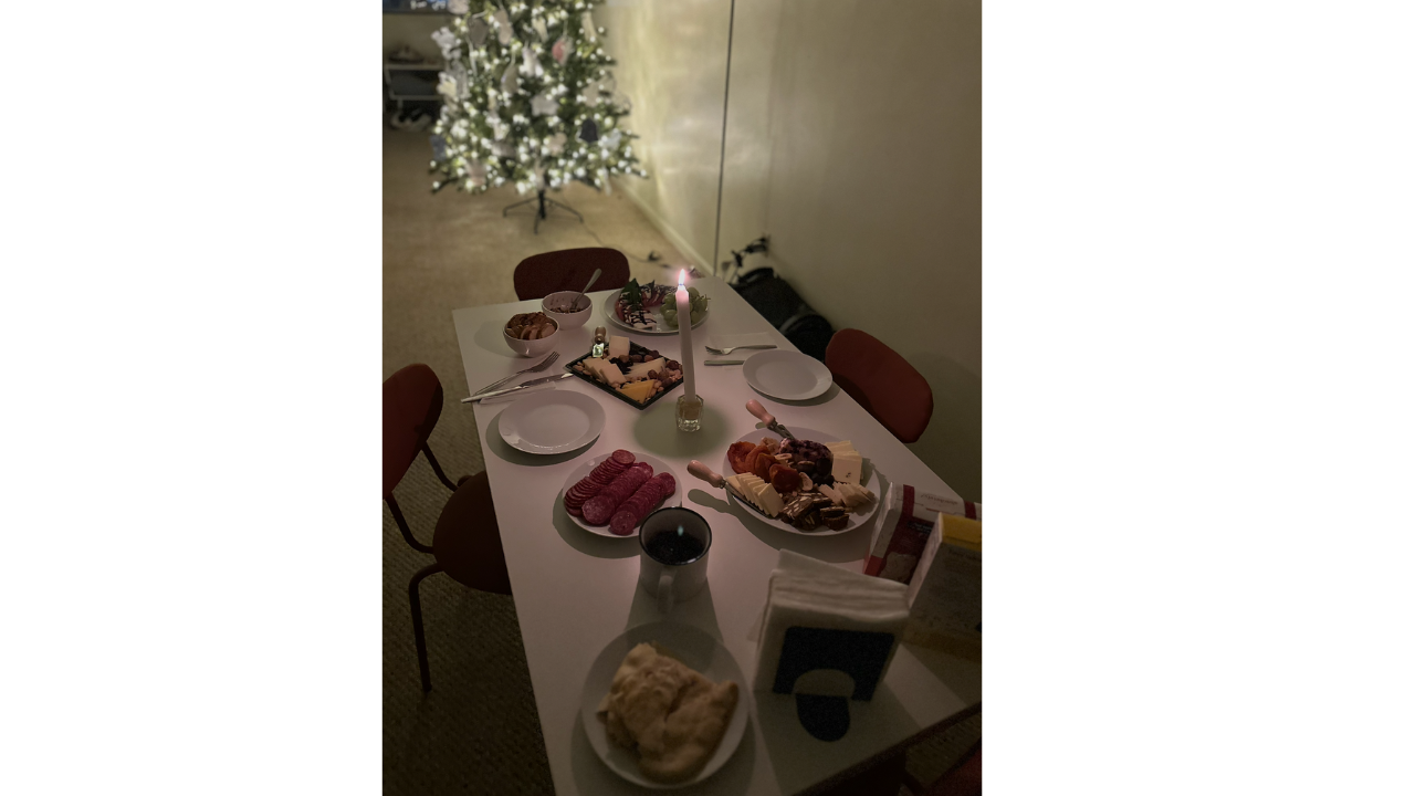 Candlelit table set for a simple Christmas meal in a quiet apartment with a lit tree in the background