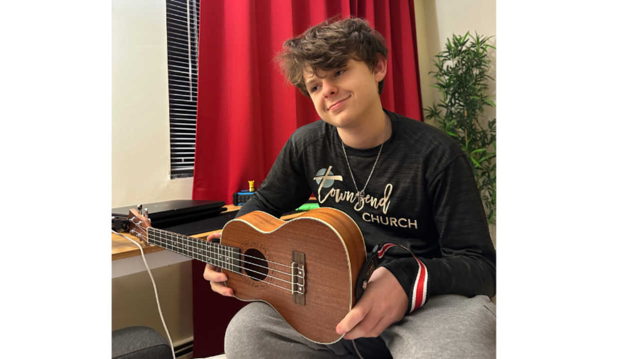 Teenage boy sitting on a bed holding a ukulele, beginning to explore music as a new form of healing and expression.