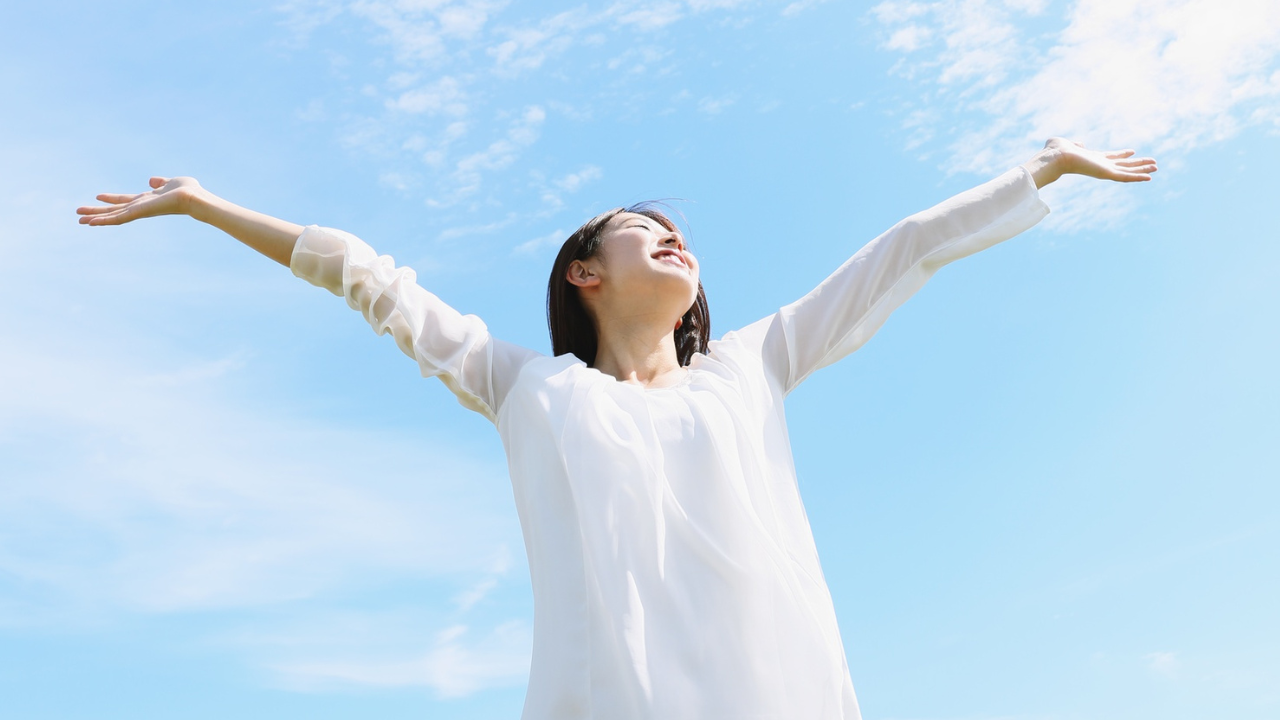 woman standing outside with her hands up in the air, experiencing a beautiful blue sky day
