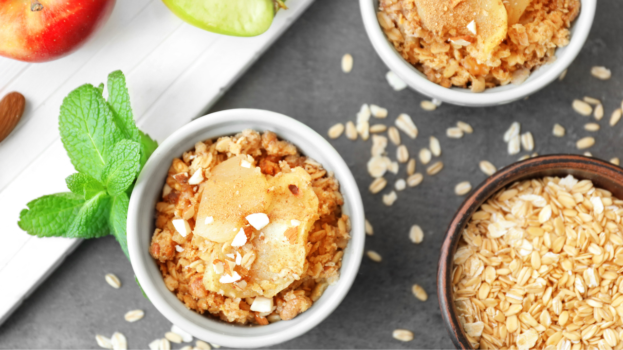 apple crisp in baking jars topped with chopped nuts, garnished with herbs and plated against chopped apples and a bowl of gluten free oats
