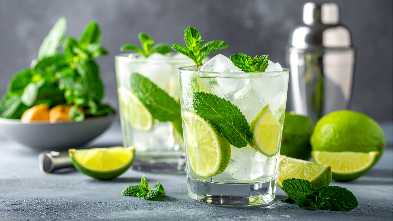 cucumber mint and lime mocktails pictured next to a cocktail shaker with lime wedges and mint garnishes