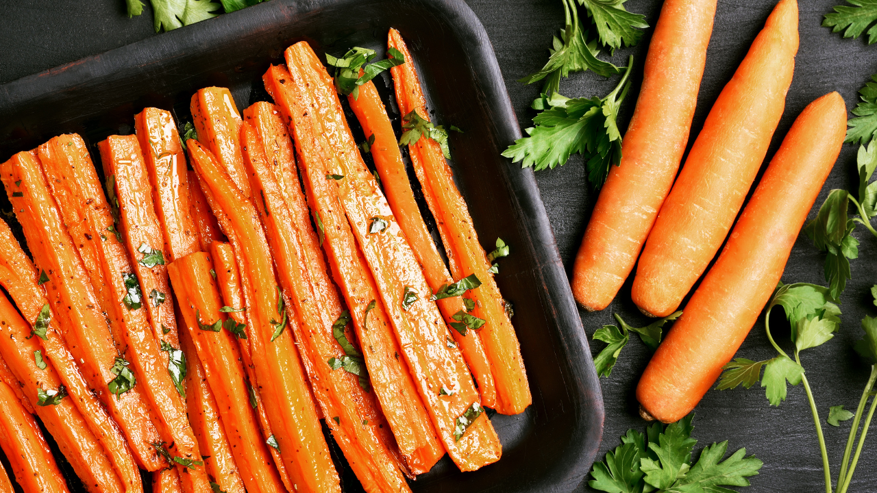Roasted carrot "fries" in a baking dish garnished with fresh herbs plated next to other herbs and carrots