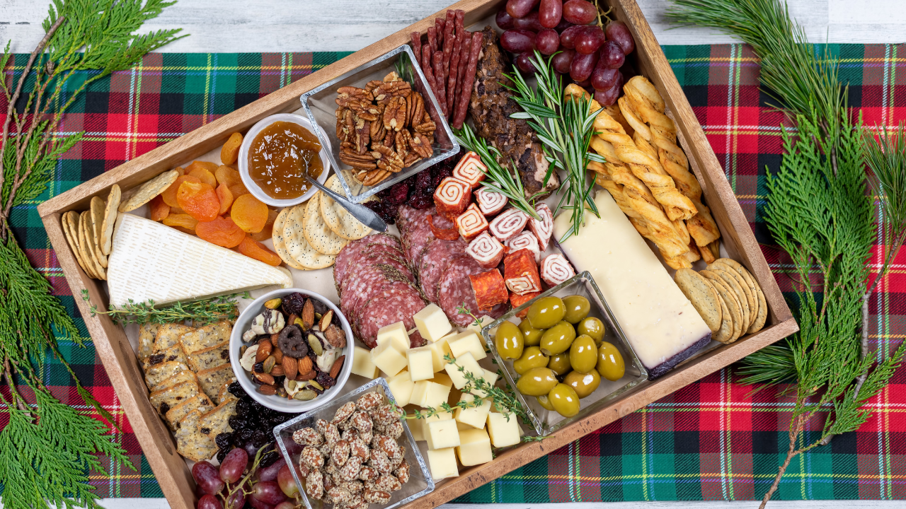 charcuterie board filled with cheeses, meats, olives, nuts, jams, etc laid out on a christmas styled table runner