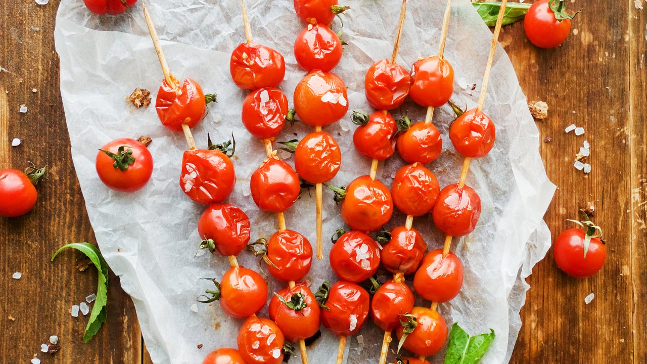 Roasted cherry tomatoes on a skewer, lined on parchment paper waiting to be drizzled with balsamic glaze