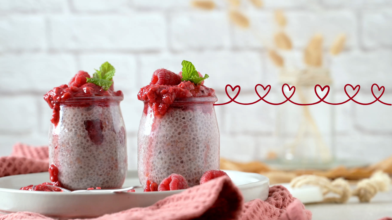 two cups of raspberry chia dessert plated with fresh raspberries and a heart graphic