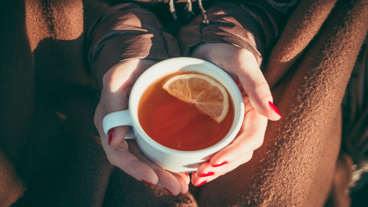 woman bundled up in a fall blanket and scarf, holding a cup of teat with a slice of lemon in it