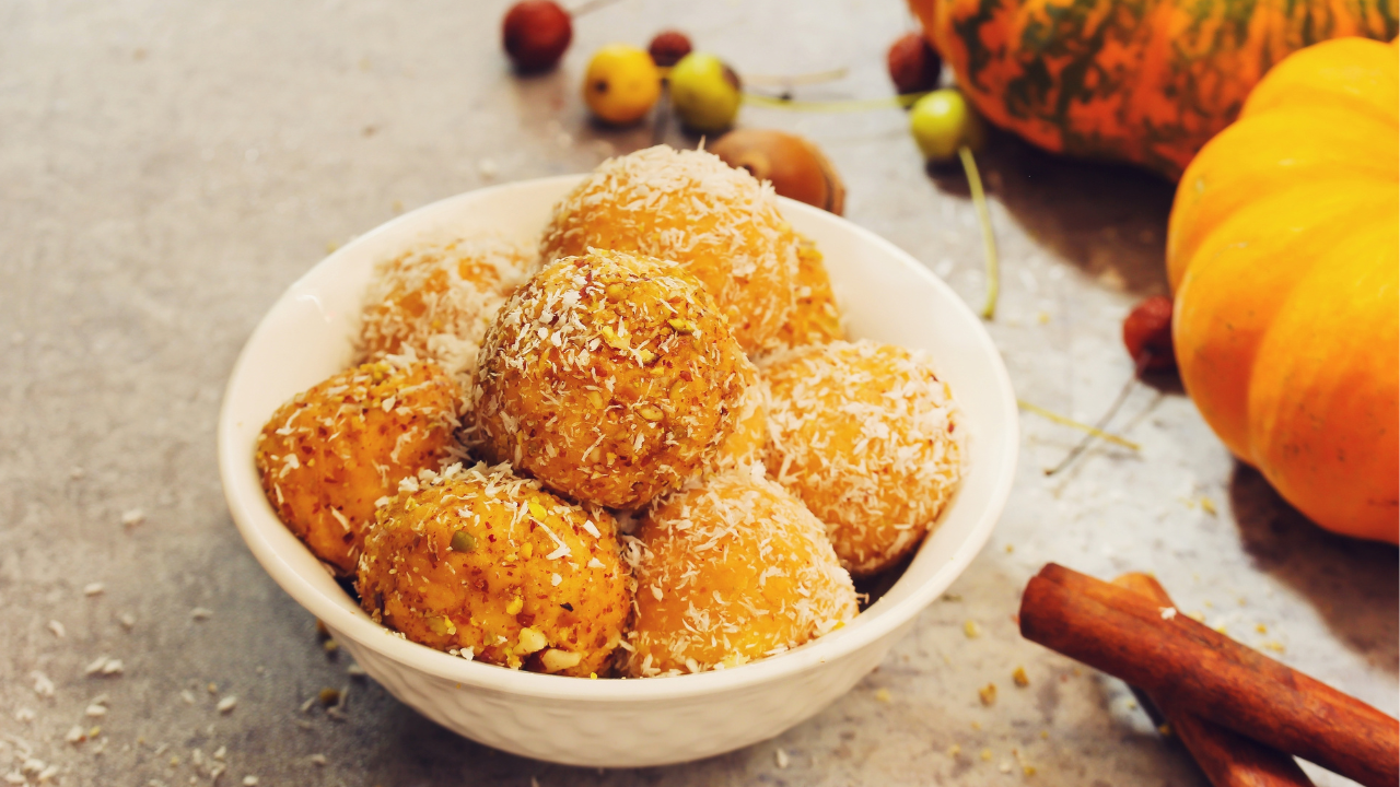 pumpkin pie bites rolled into balls, sprinkled with shredded coconut flakes, styled next to pumpkins and cinnamon sticks