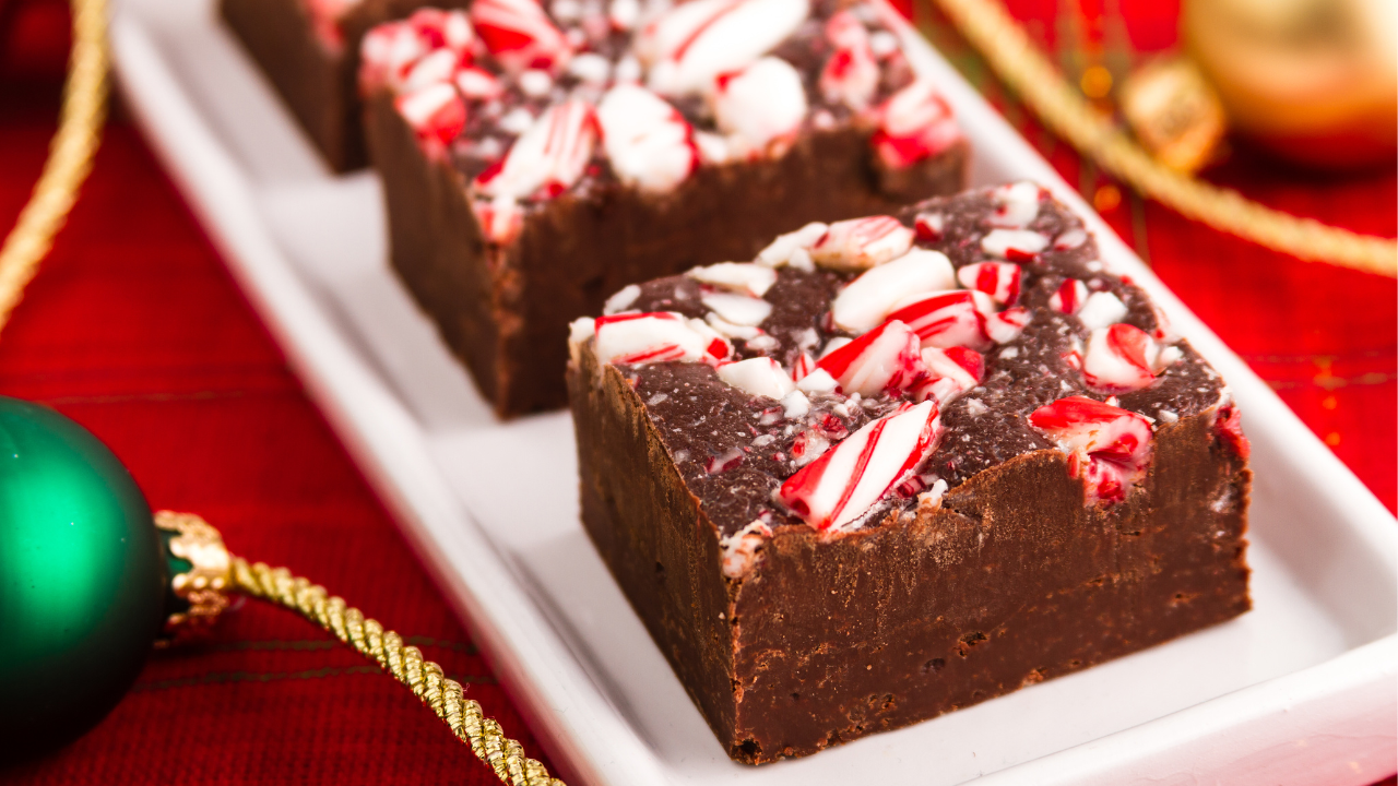 Fudge bars topped with crushed peppermint lined on a glass tray pictured next to ornaments and Christmas decor 