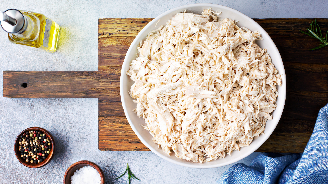 big bowl of shredded chicken placed next to seasonings and olive oil