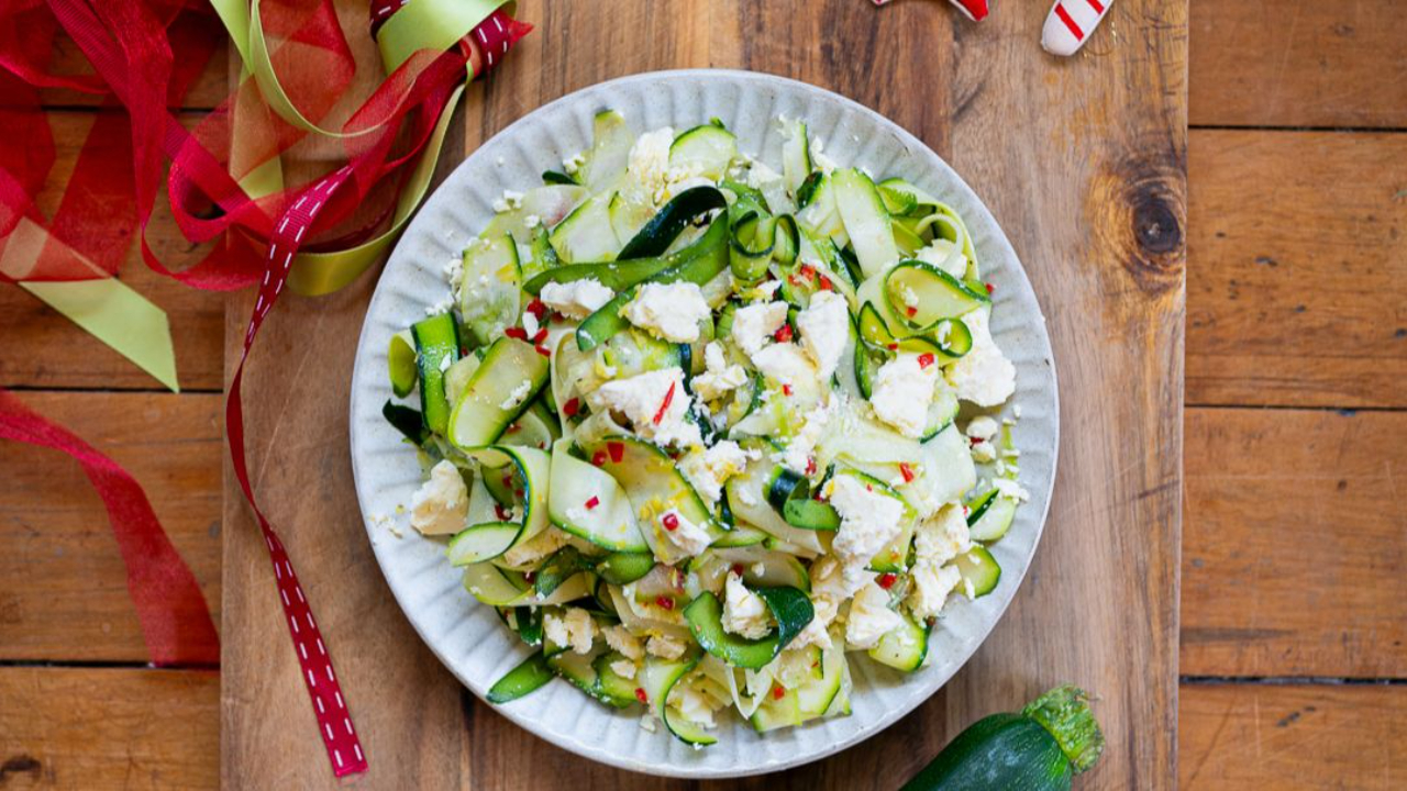 fresh courgette ribbons with crumbled feta cheese and red chilli in white serving plate