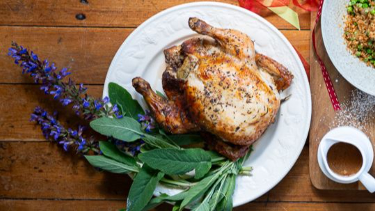 golden roasted stuffed chicken on serving platter with fresh sage garnish and gravy jug