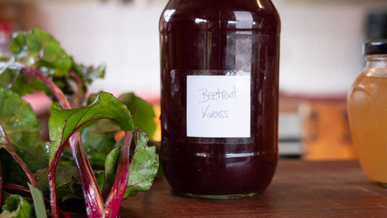 deep red beetroot kvass in a glass jar with fresh beetroot leaves on a wooden board